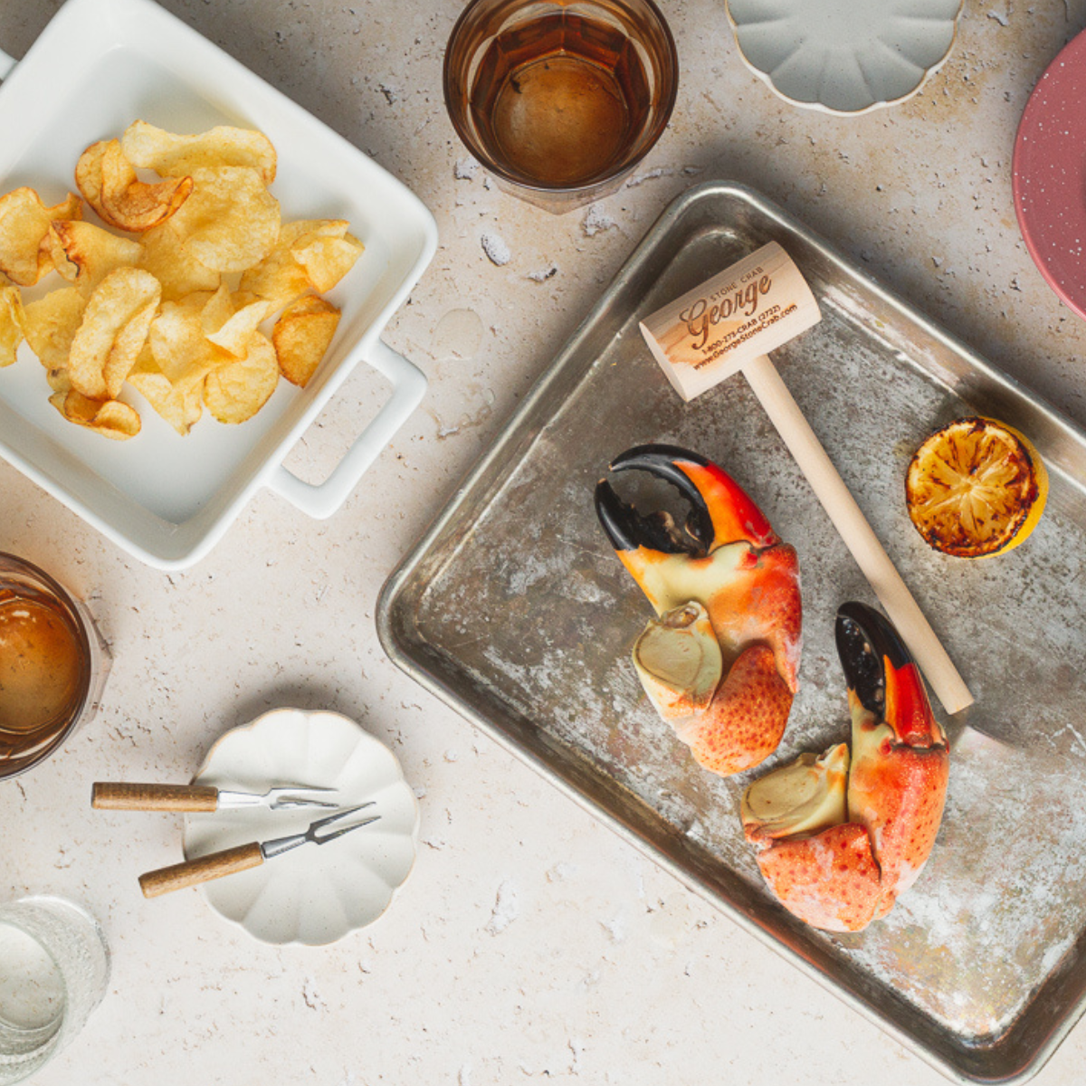 Two stone crab claws sitting on ice with an imprinted George Stone Crab mallet, with potato chips on a side dish