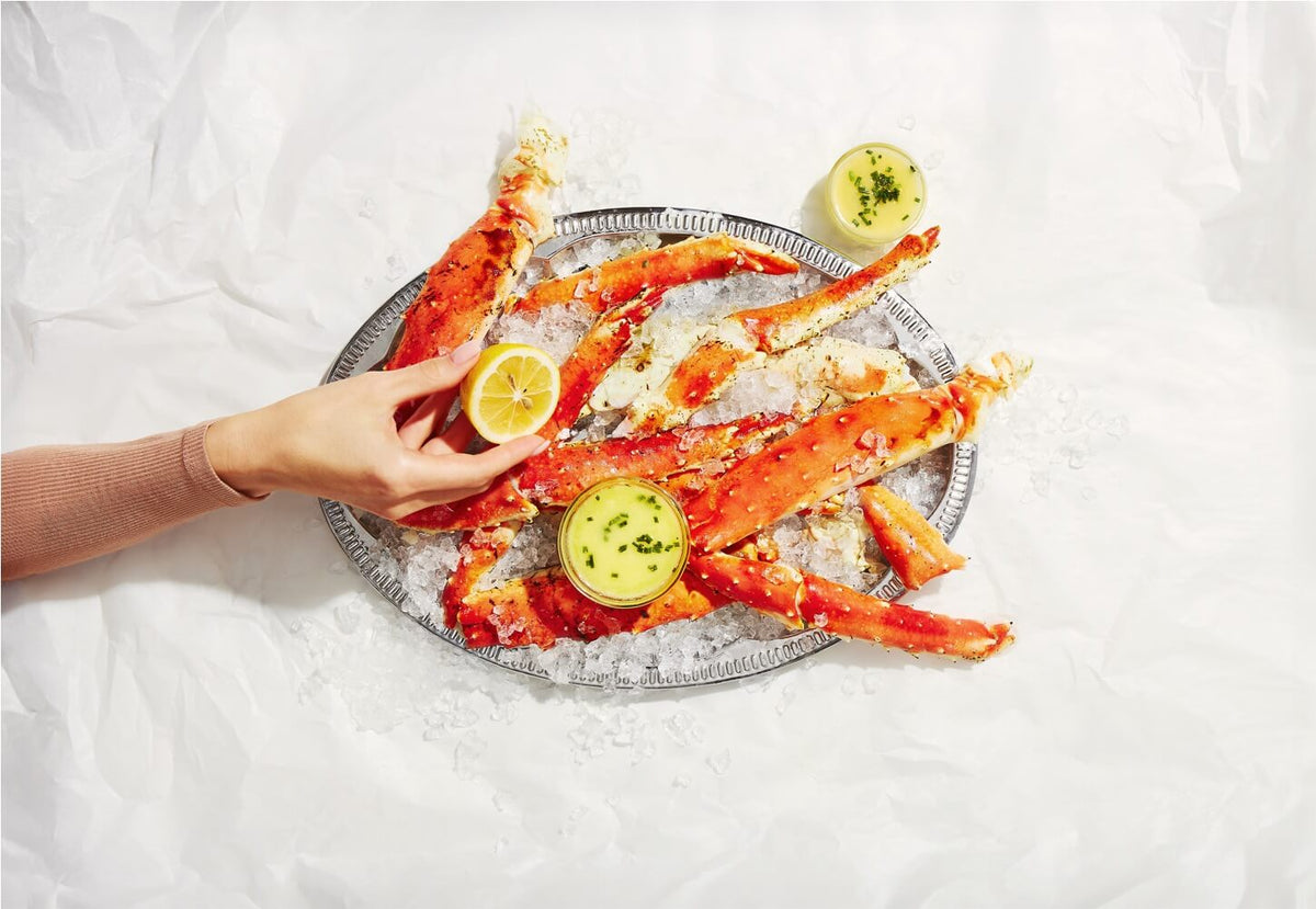 Person holding a tray of crab legs with lemon wedges on a white surface