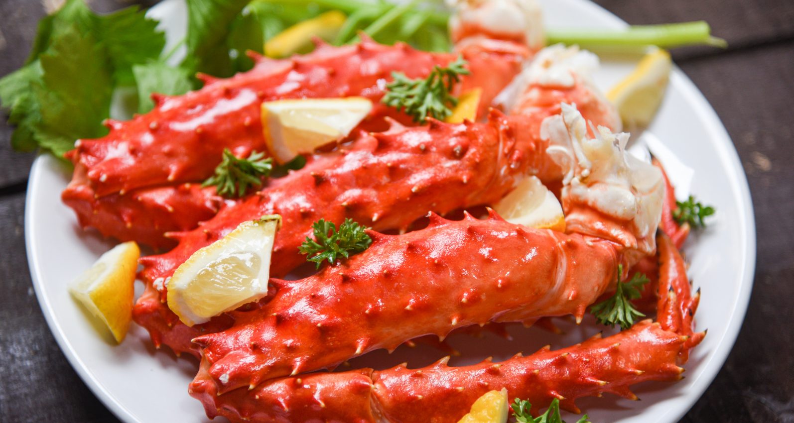 Plated red crab legs garnished with lemon wedges and parsley on a white plate.