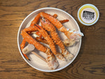 White plate with alaskan king crab legs and a container of butter sauce on a wooden surface.