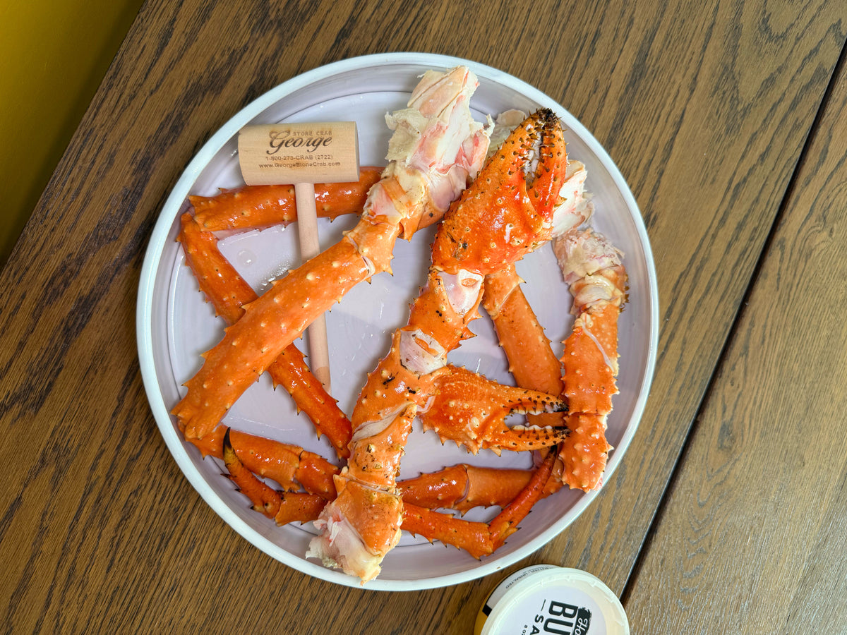 Raw crab legs on a white plate with a wooden background